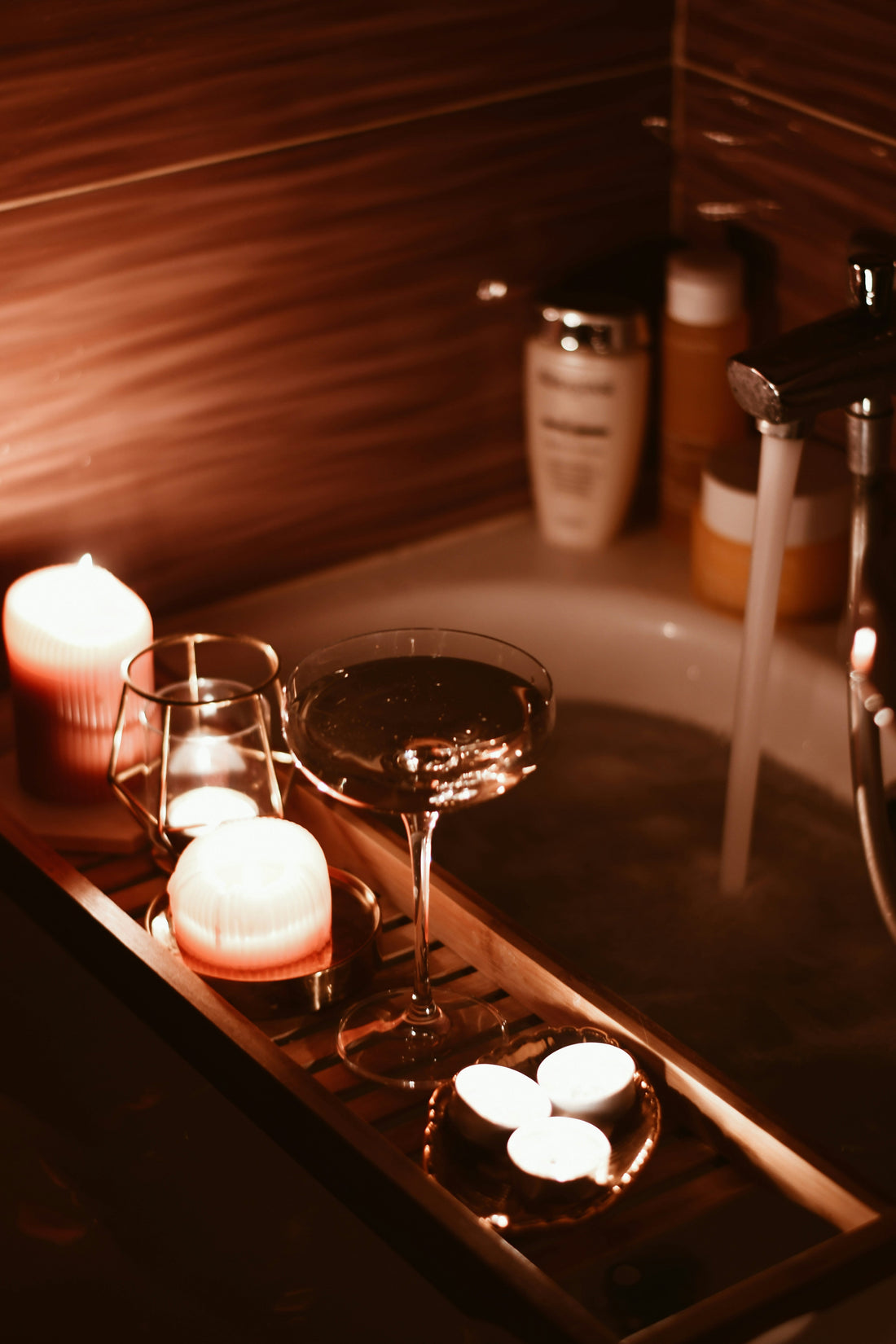 Candles and wine glass on a wooden bath tray in warm evening light