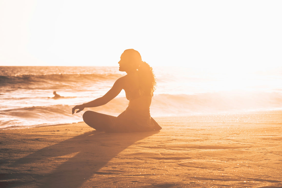 Woman meditating on beach in golden sunset light
